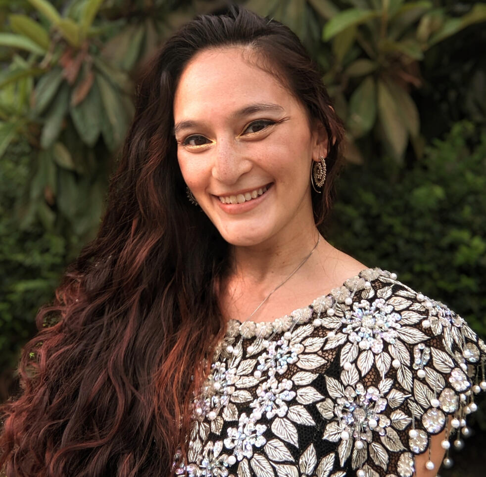 Headshot of the Author, long wavy dark haired woman wearing a beaded black and white top