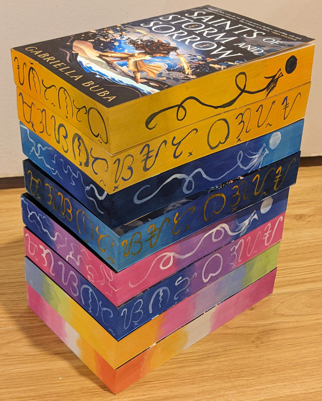 Images of 3 custom edge painted copies of Saints of Storm and Sorrow with bi flag colors, lesbian flag colors, and the rainbow flag